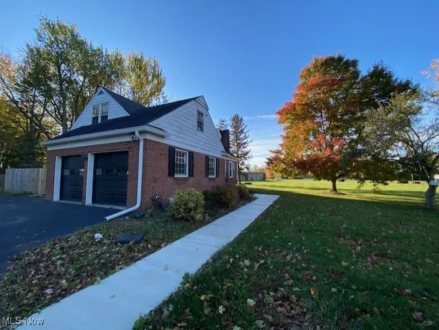 View of property exterior with a lawn, brick siding, an attached garage, and asphalt driveway