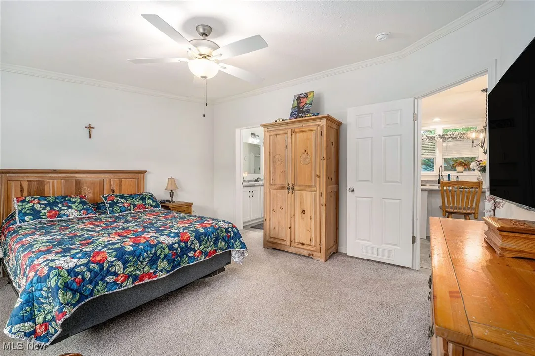 Bedroom with crown molding, light colored carpet, ceiling fan, and ensuite bath