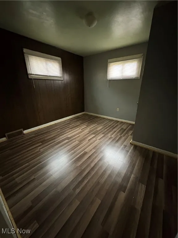 Spare room with healthy amount of natural light, wood walls, and dark wood-style flooring