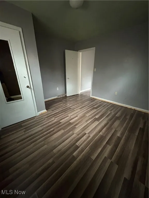 Unfurnished bedroom featuring dark wood-type flooring and baseboards