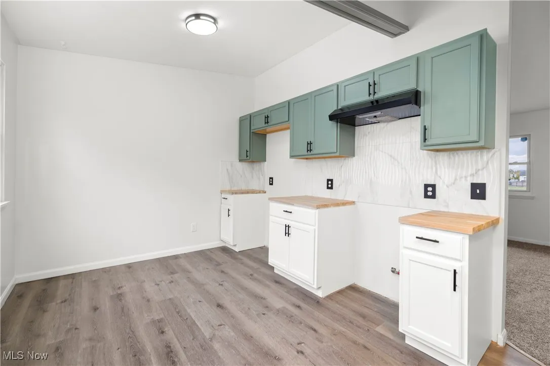Kitchen with under cabinet range hood, tasteful backsplash, light wood-type flooring, and wood counters