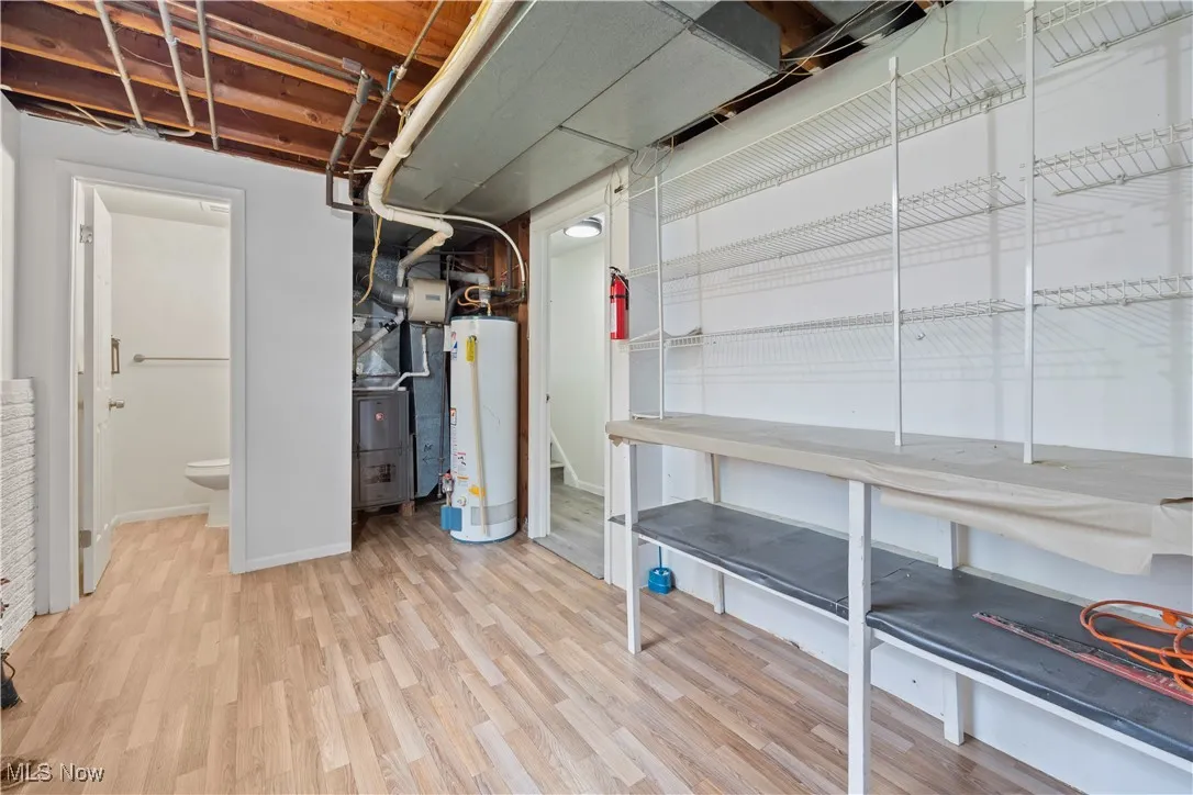 Unfinished below grade area with light wood-style floors, water heater, and heating unit