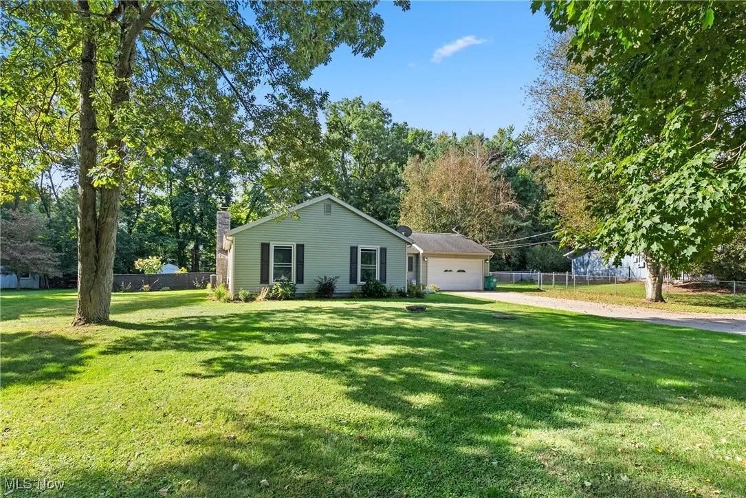Single story home featuring driveway, a chimney, a garage, and view of scattered trees