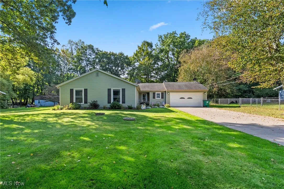 Single story home with driveway, a garage, and view of wooded area