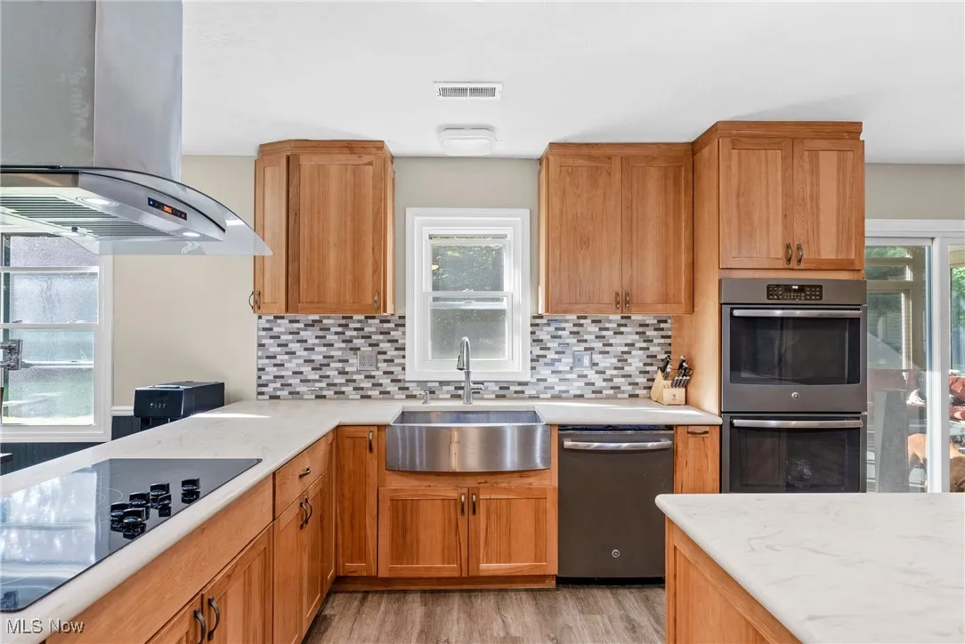 Kitchen featuring island range hood, decorative backsplash, stainless steel appliances, and brown cabinets