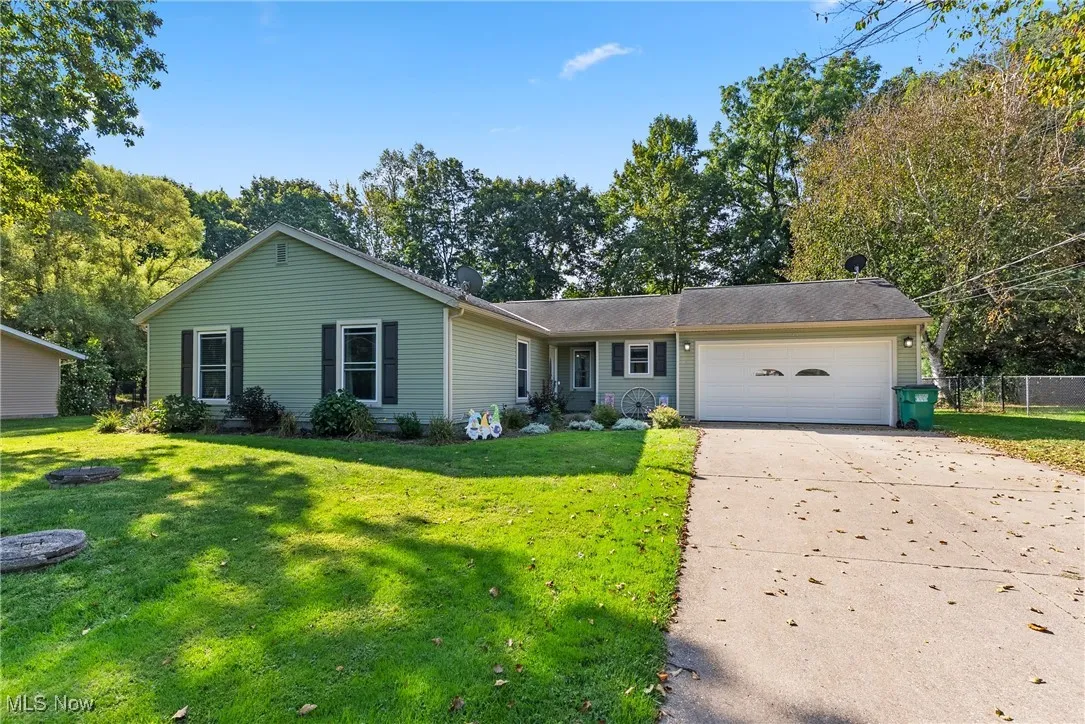 Ranch-style home with concrete driveway, an attached garage, and view of scattered trees