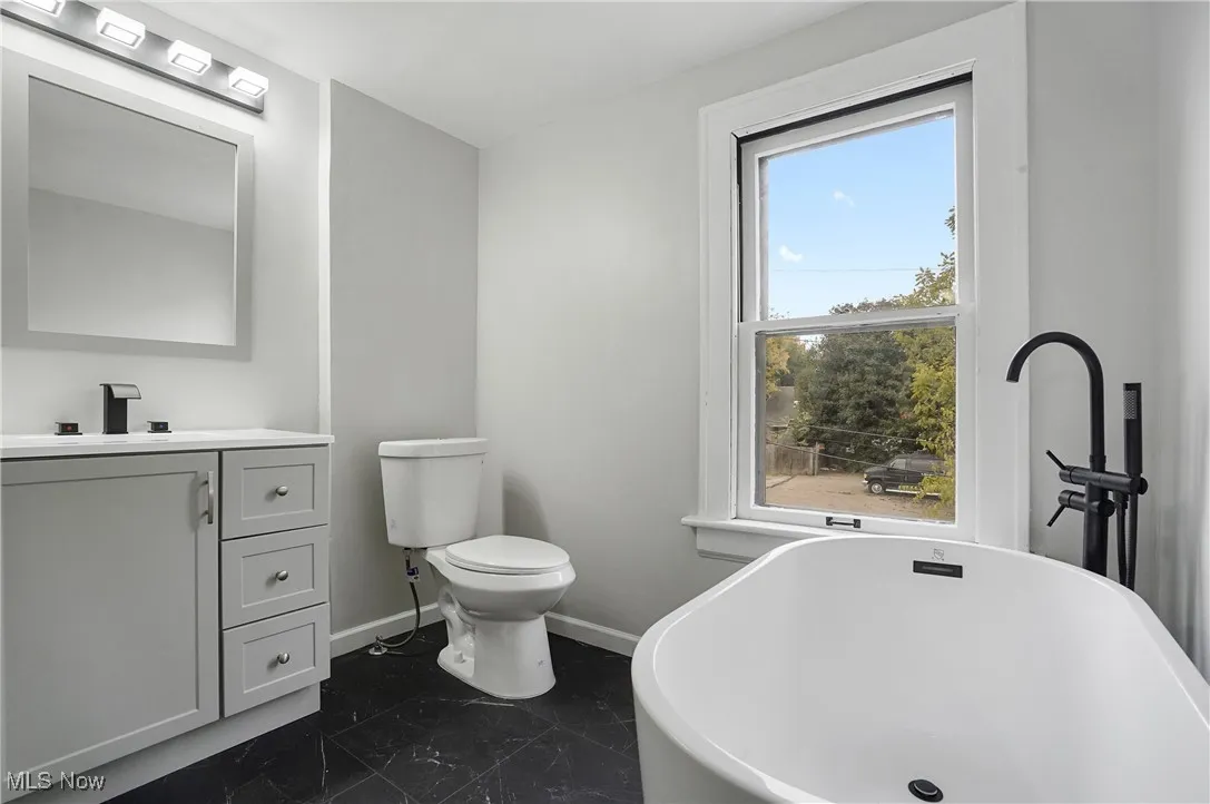 Full bath featuring a freestanding bath, vanity, and dark marble finish floors
