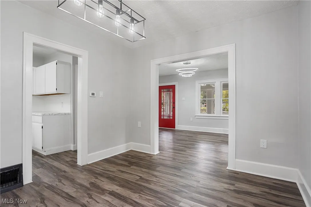 Unfurnished dining area featuring a textured ceiling, dark wood-style flooring, and a chandelier