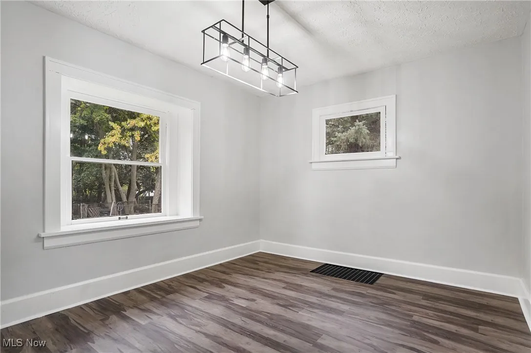 Unfurnished dining area featuring a textured ceiling, dark wood-style flooring, plenty of natural light, and a chandelier