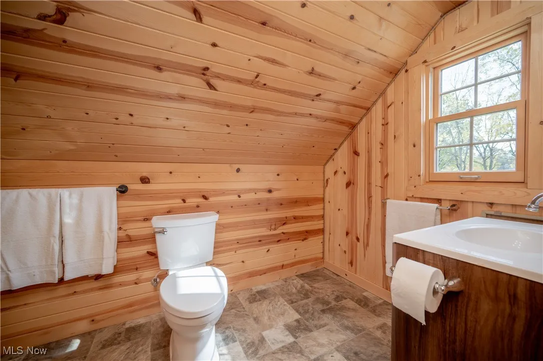 Bathroom featuring vanity, lofted ceiling, wooden walls, wooden ceiling, and stone finish flooring