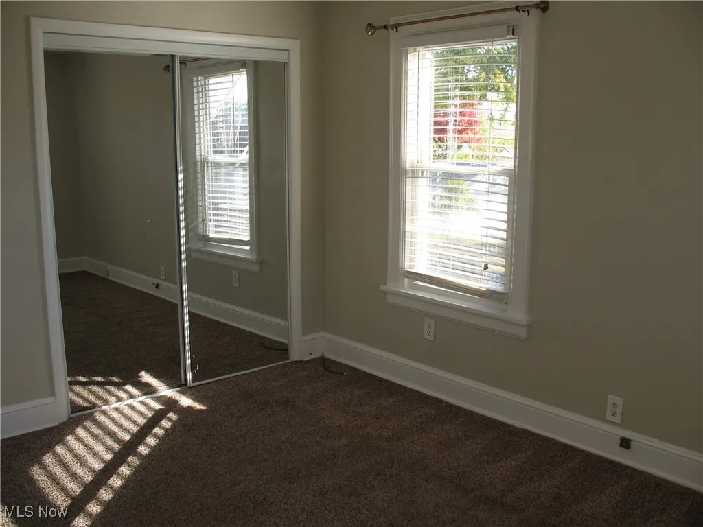 Unfurnished bedroom featuring a closet, dark colored carpet, and multiple windows