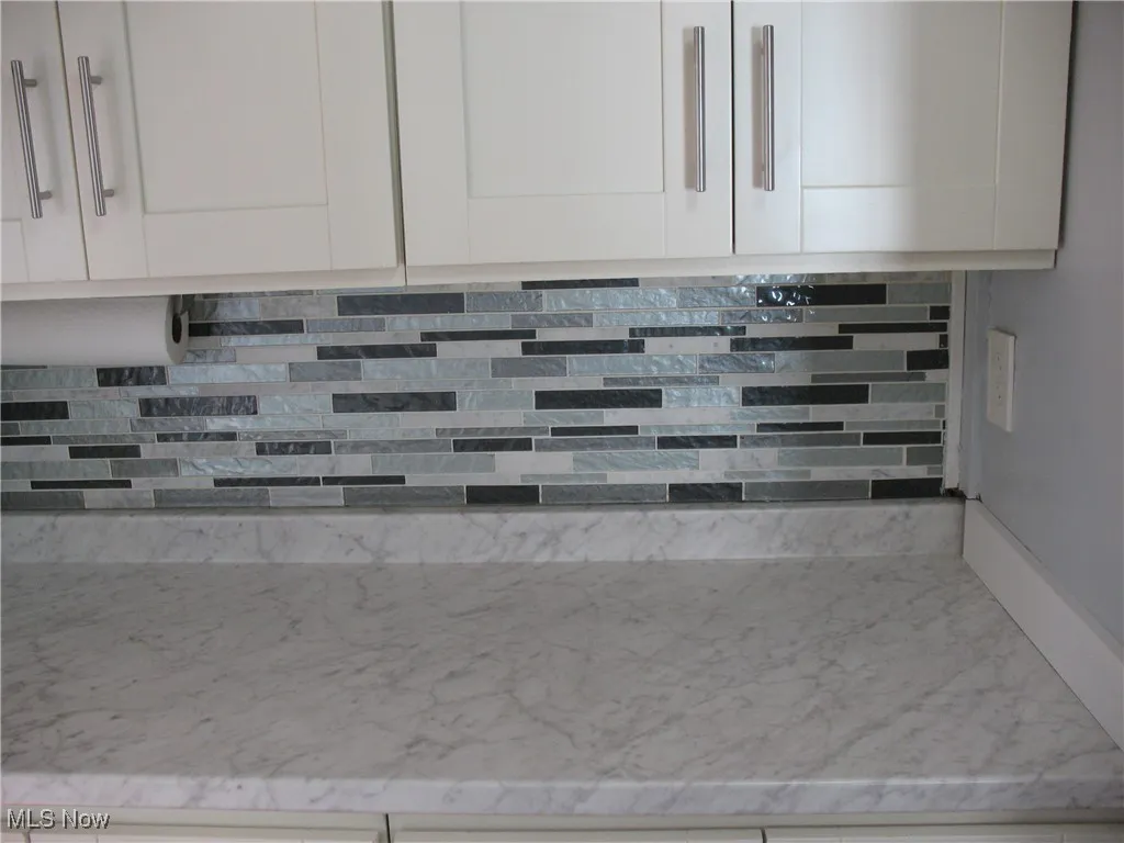 Kitchen view of light stone countertops, white cabinets, and decorative backsplash