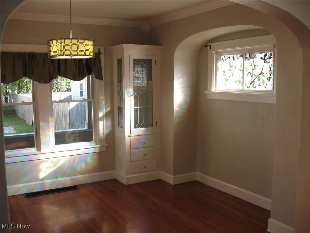 Unfurnished dining area featuring arched walkways, plenty of natural light, dark wood-type flooring, and ornamental molding