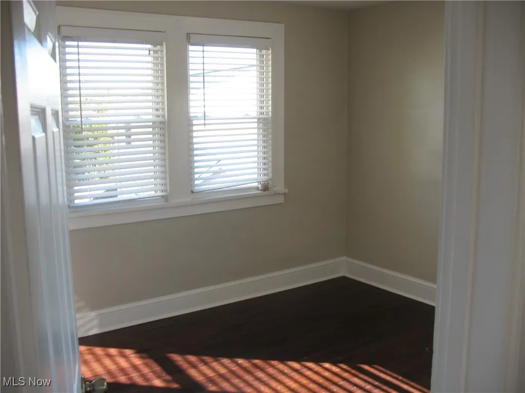 Unfurnished room with baseboards and dark wood-type flooring