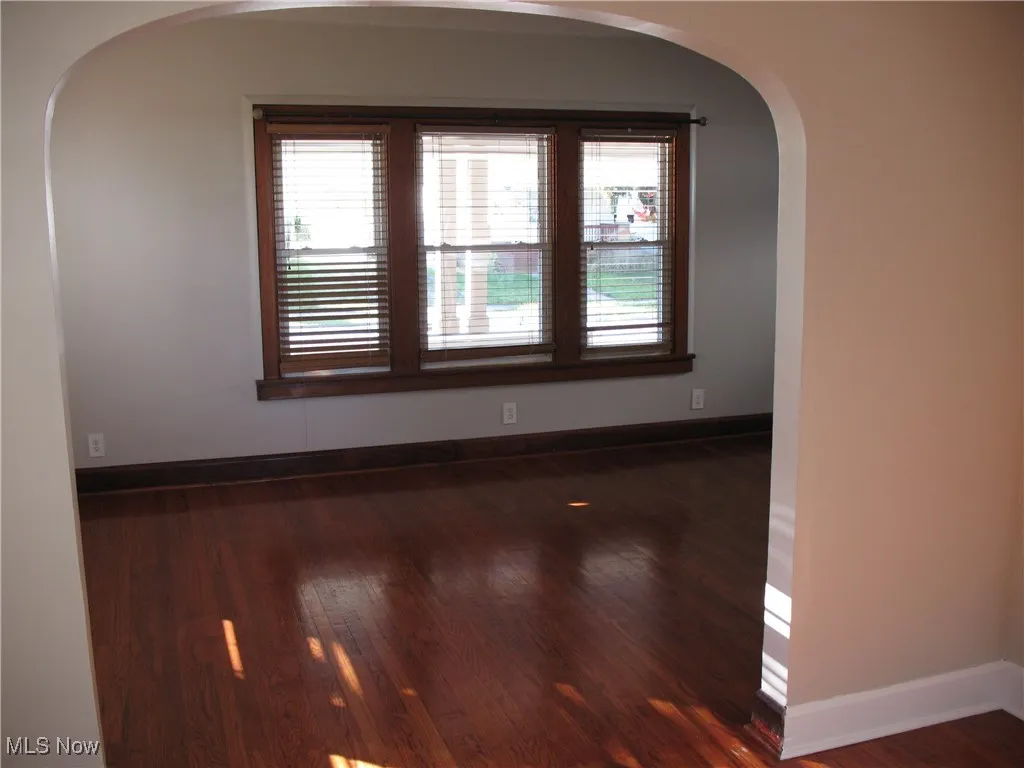 Unfurnished room featuring arched walkways and dark wood finished floors