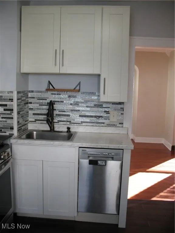 Kitchen featuring light countertops, white cabinetry, stainless steel dishwasher, and dark wood-type flooring