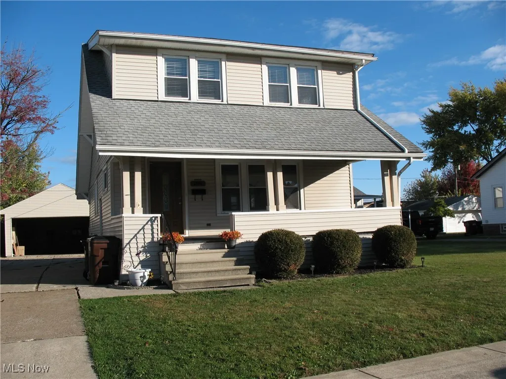 View of front of property with covered porch, a front lawn, a garage, a shingled roof, and an outdoor structure