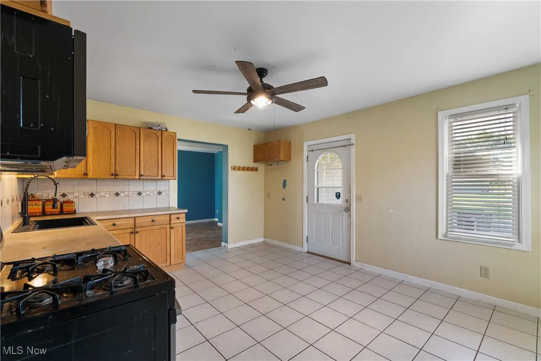 Kitchen with black appliances, backsplash, light tile patterned floors, and plenty of natural light