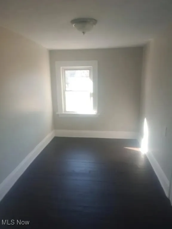 Empty room featuring baseboards and dark wood-type flooring
