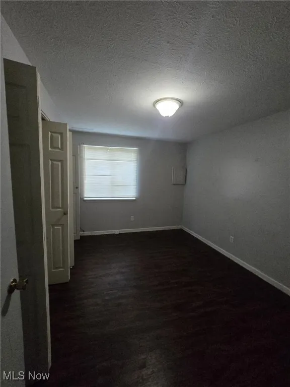 Unfurnished room featuring dark wood-style flooring and a textured ceiling