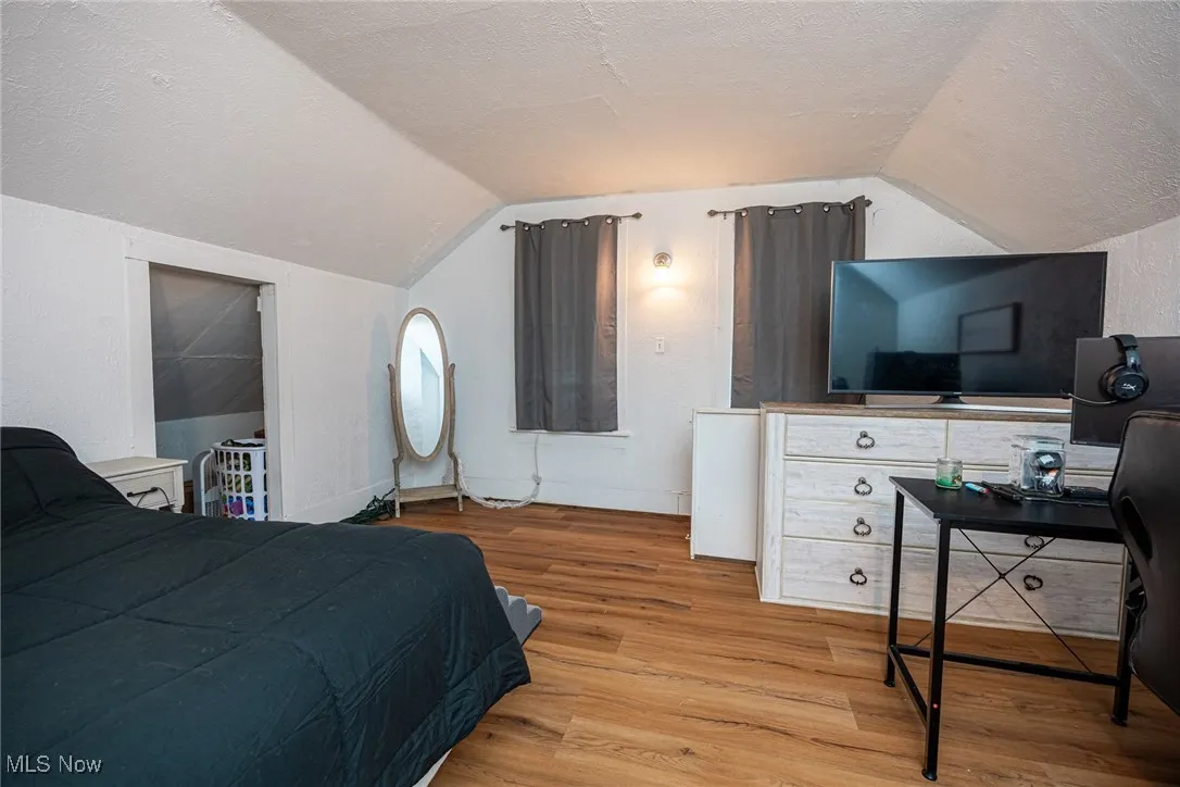 Bedroom with a textured ceiling, light wood-style flooring, lofted ceiling, and an office area