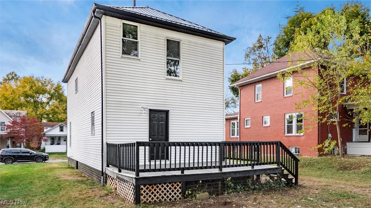 Back of property featuring a wooden deck, a lawn, a metal roof, and a standing seam roof