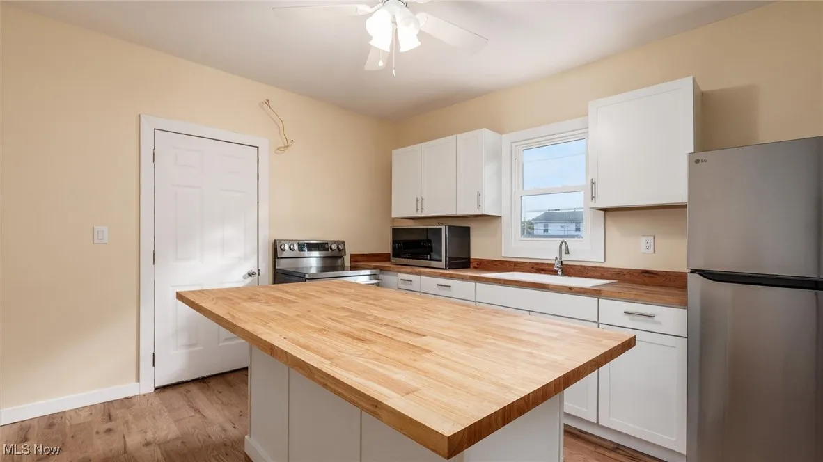 Kitchen featuring stainless steel appliances, white cabinetry, wooden counters, and light wood-style flooring