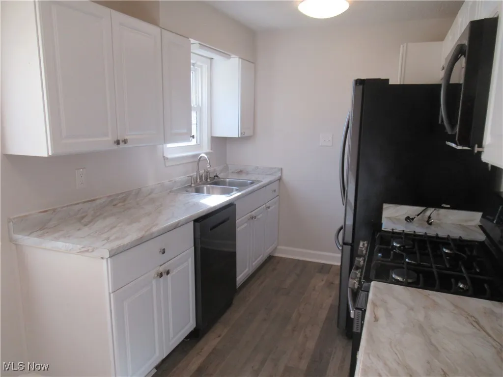 Kitchen featuring light countertops, white cabinets, black appliances, and dark wood-type flooring