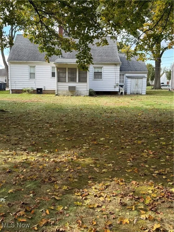 Rear view of house featuring a yard, a sunroom, a chimney, and a shingled roof