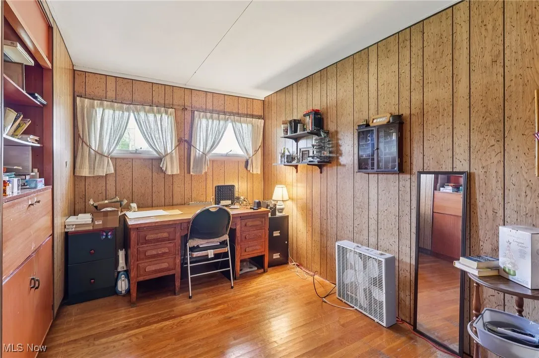 Home office with light wood-style flooring, wood walls, and heating unit