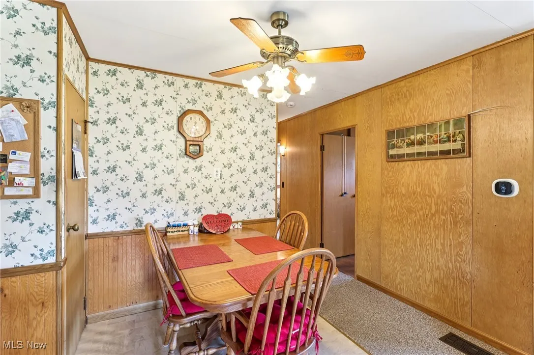 Dining space featuring wood walls, crown molding, wainscoting, and a ceiling fan