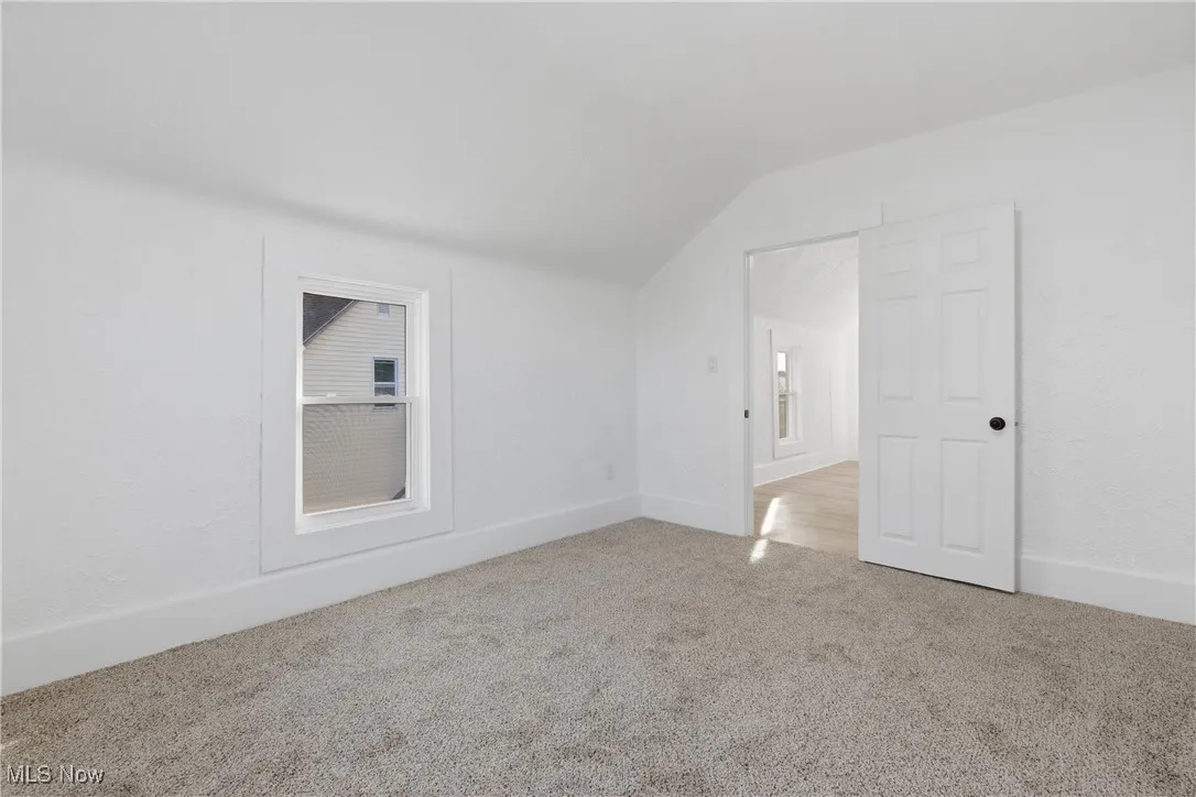 Carpeted empty room with vaulted ceiling and baseboards