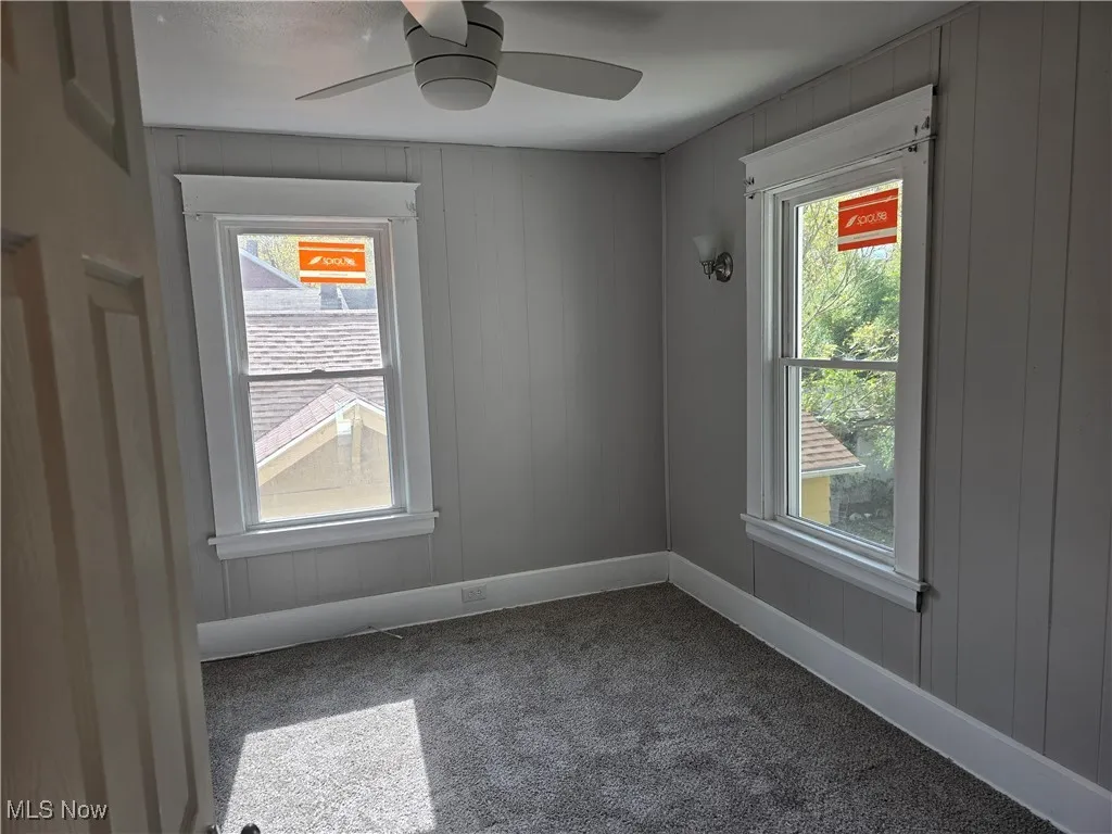 Unfurnished room featuring carpet flooring, wooden walls, plenty of natural light, and a ceiling fan