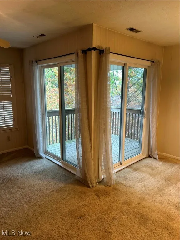 Doorway to outside with carpet flooring, a textured ceiling, and wooden walls
