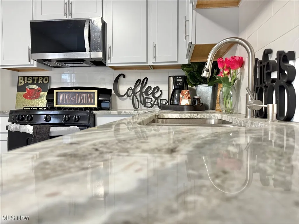 Kitchen featuring black range with gas cooktop, backsplash, stainless steel microwave, and light stone counters