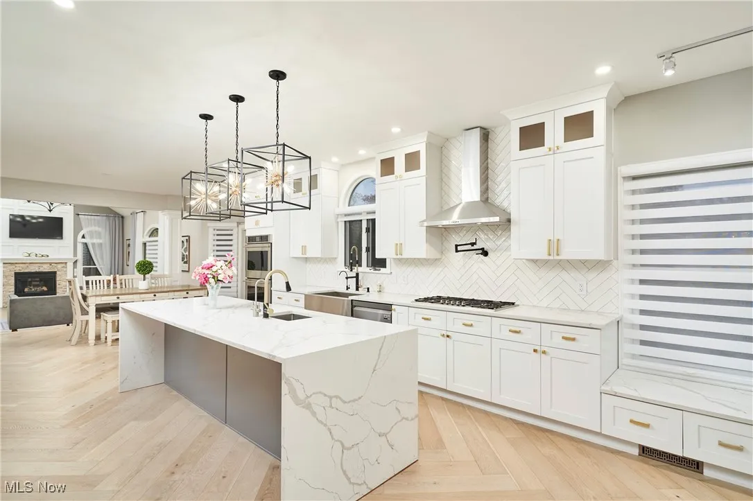 Kitchen with open floor plan, tasteful backsplash, decorative light fixtures, light stone counters, and wall chimney exhaust hood