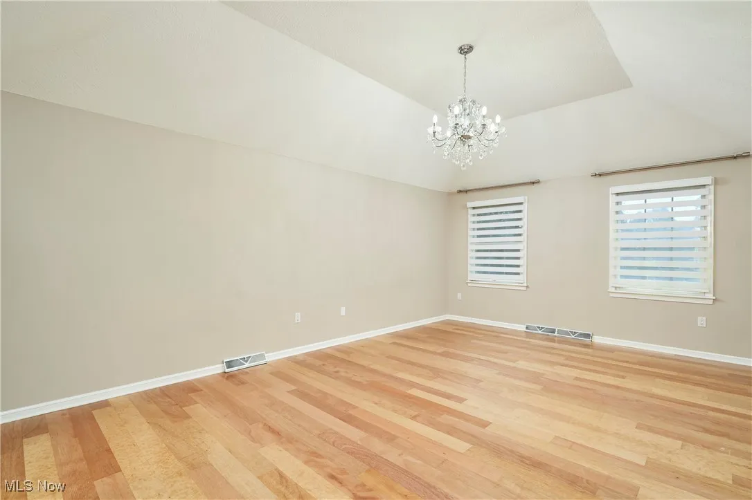 Empty room featuring a chandelier, light wood finished floors, and a tray ceiling
