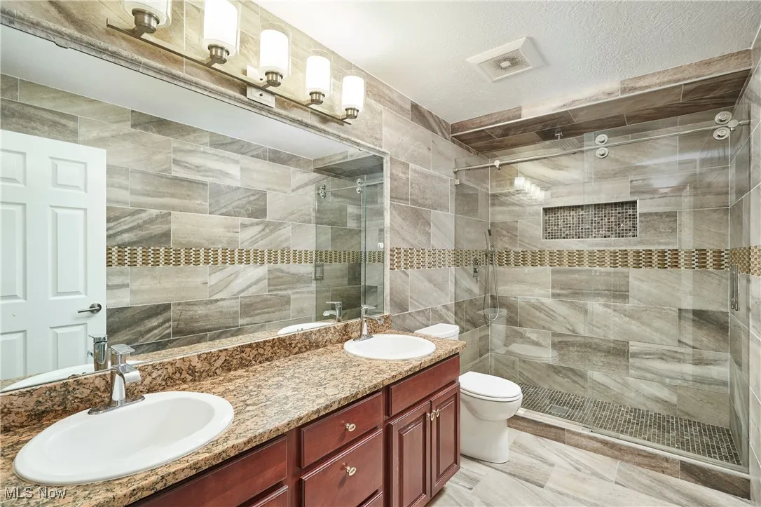 Bathroom featuring double vanity, a tile shower, tile walls, and a textured ceiling