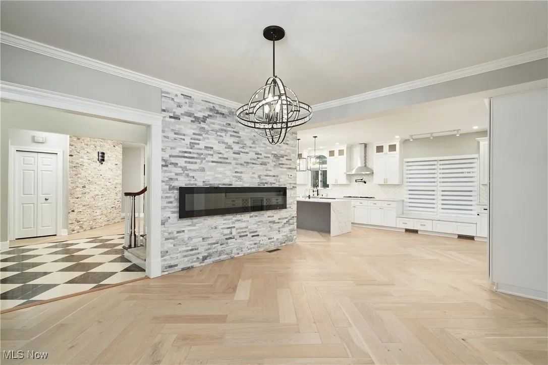 Unfurnished living room featuring ornamental molding, a chandelier, stairs, and a tiled fireplace