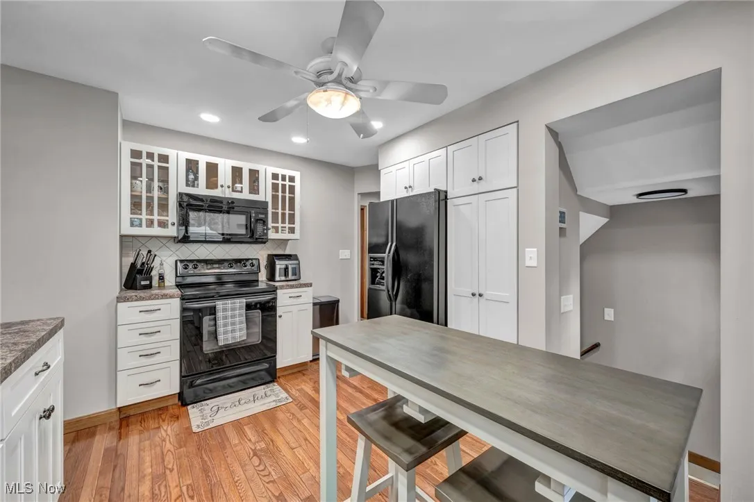 Kitchen featuring black appliances, backsplash, white cabinets, light wood-style floors, and glass insert cabinets