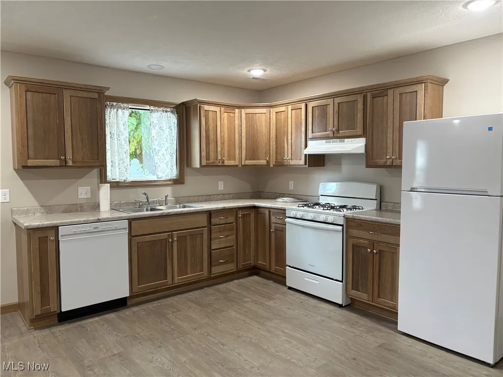 Kitchen featuring white appliances, light countertops, light wood-style flooring, under cabinet range hood, and recessed lighting