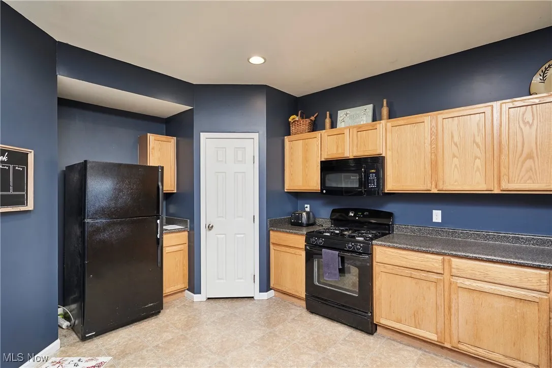 Kitchen featuring light wood cabinetry, black appliances, dark countertops, and recessed lighting
