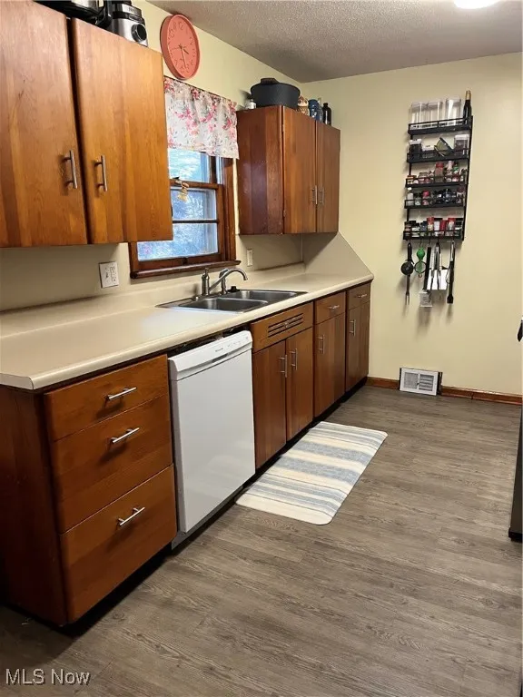 Kitchen with light countertops, dark wood-type flooring, dishwashing machine, a textured ceiling, and brown cabinets