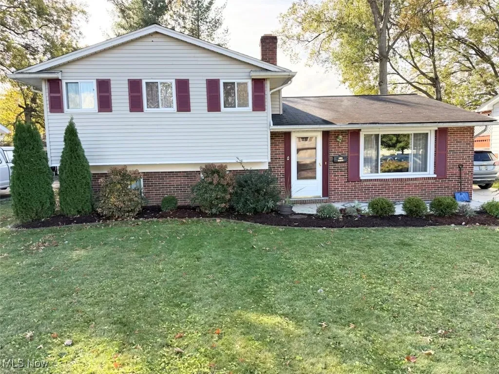 Split level home with a chimney, a front lawn, and brick siding