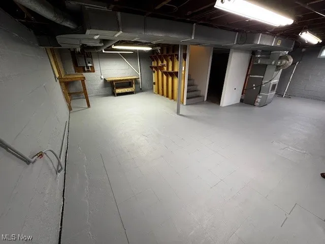 Unfinished basement featuring tile patterned floors, stairs, and heating unit