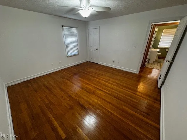 Unfurnished bedroom with a textured ceiling, dark wood finished floors, and ceiling fan