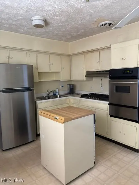Kitchen featuring light floors, appliances with stainless steel finishes, a textured ceiling, a warming drawer, and a center island