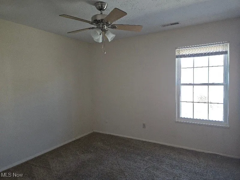 Unfurnished room featuring a textured ceiling, ceiling fan, and dark colored carpet