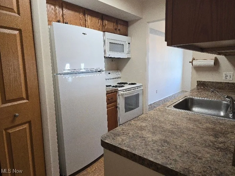 Kitchen featuring dark countertops, white appliances, and brown cabinetry