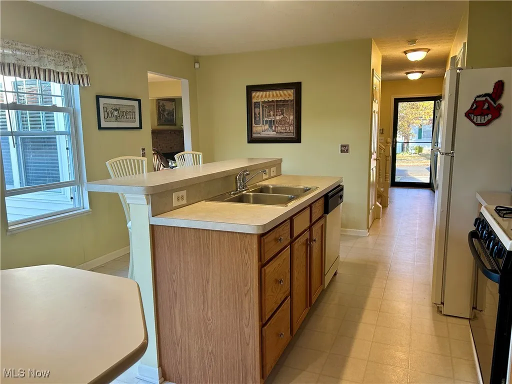 Kitchen featuring a kitchen island with sink, gas stove, light countertops, brown cabinets, and dishwasher